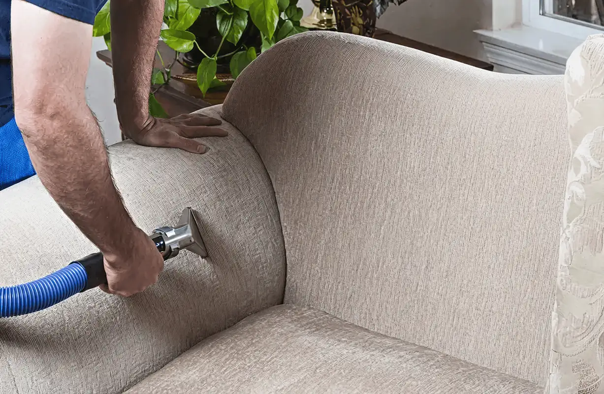Professional upholstery cleaner deep-cleaning a fabric sofa with a handheld extraction tool and hose, Grand Rapids, MI.